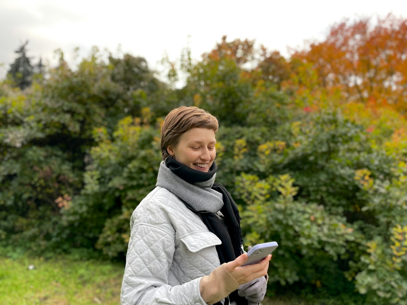 Kvinna i höstjacka ler mot sin mobil utomhus
