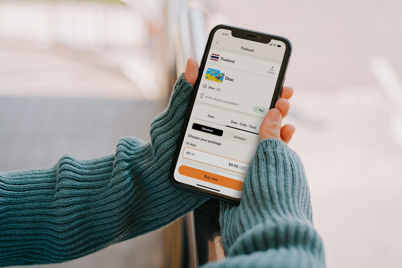 Hand som håller en mobil med en reseapp i en stickad tröja