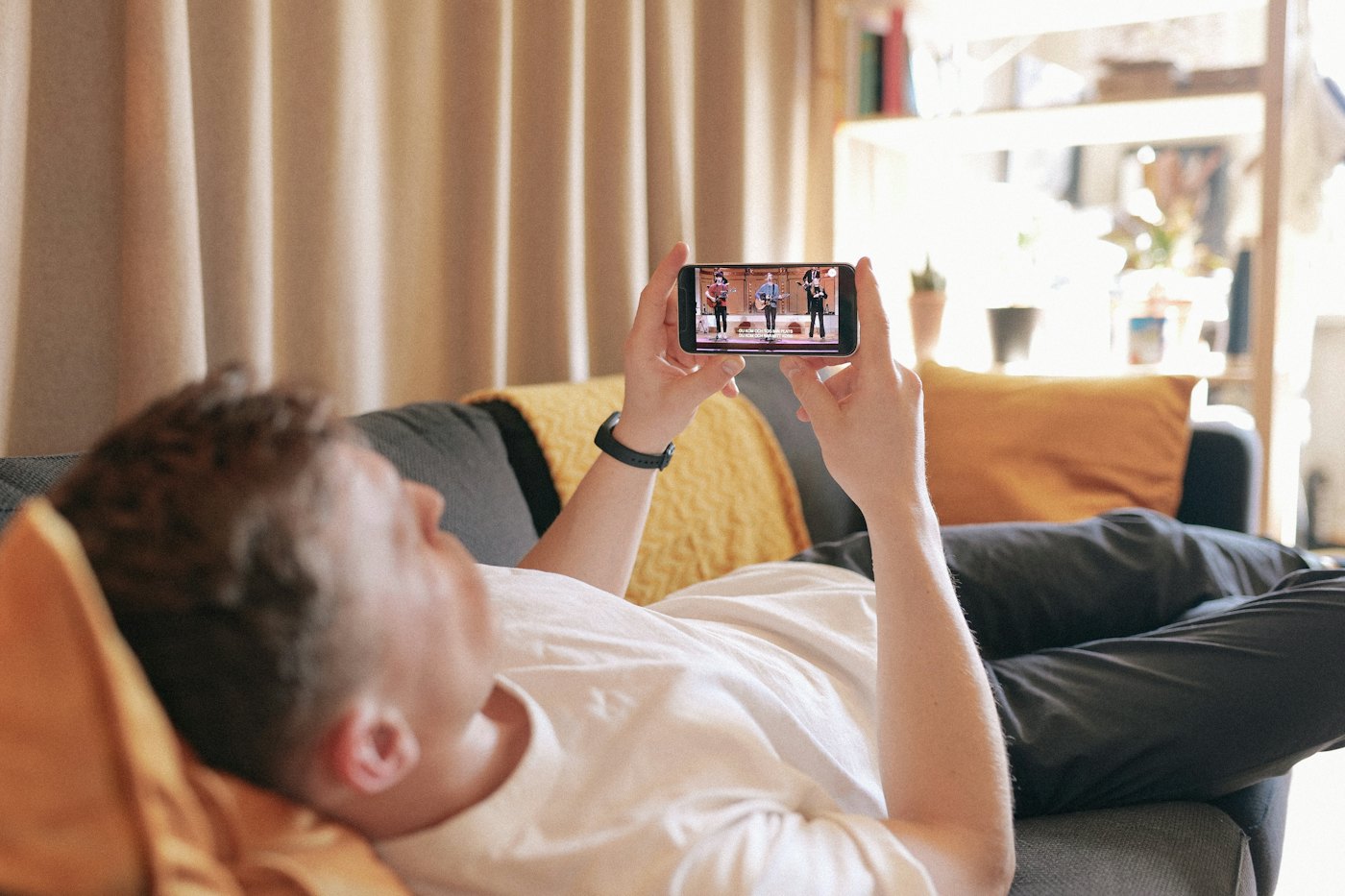 Man som ligger i soffan och tittar på video i mobilen
