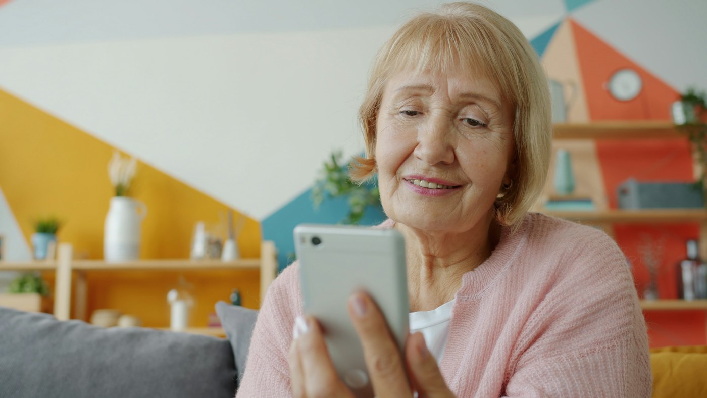 Äldre kvinna som ler mot sin mobil